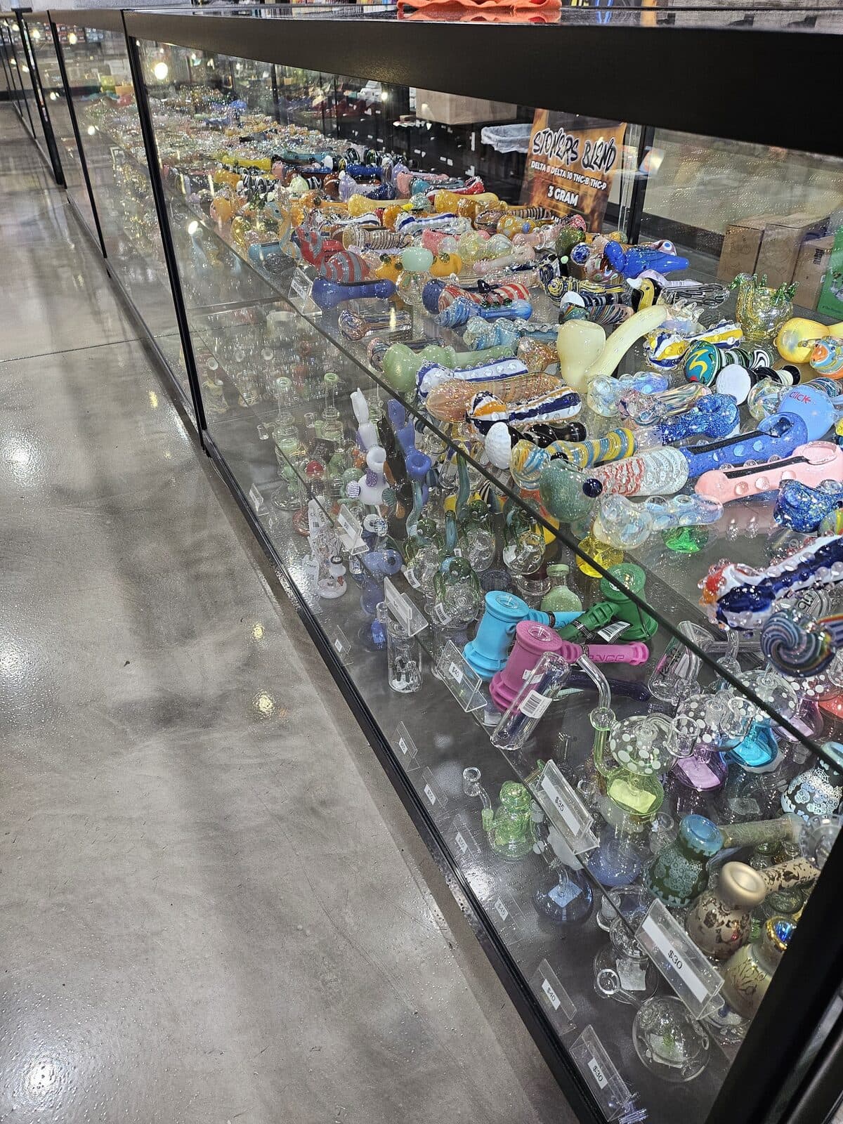 Long lit display case packed with American-made hand pipes and rigs at 3 Heads Smoke Shop in Elgin